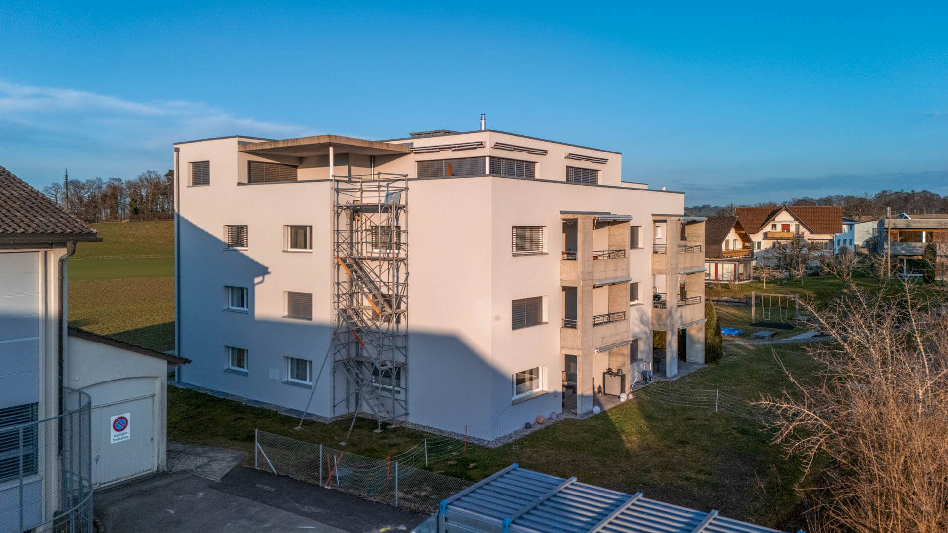 Fertig gestrichene Fassade eines Mehrfamilienhauses mit Gerüst-Treppenturm – Foto: KUGE Bau AG